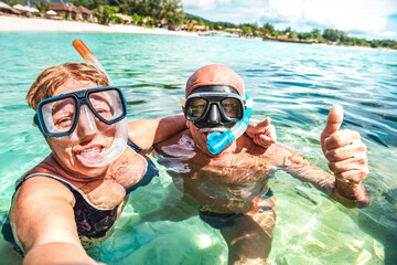 Senior couple taking happy selfie at tropical sea excursion with water camera - Boat trip snorkeling concept in exotic scenarios - Active retired life and fun around the world - Bright vivid filter - 583496945