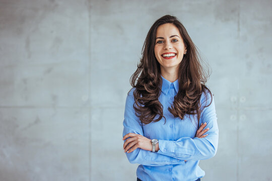 Portrait of beautiful confident smiling businesswoman standing with arms crossed in the office and looking at camera. Cropped portrait of an attractive young businesswoman standing alone