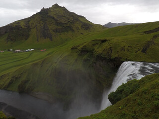 Scenic view of a waterfall and a green meadow under a gray sky in Iceland
