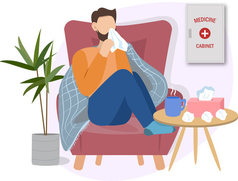 sick man possibly with cold or flu is at home on a sofa having a cup of tea or hot drink