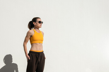 Fit, sporty, toned woman wearing a sports bra and tracksuit bottoms and sunglasses.