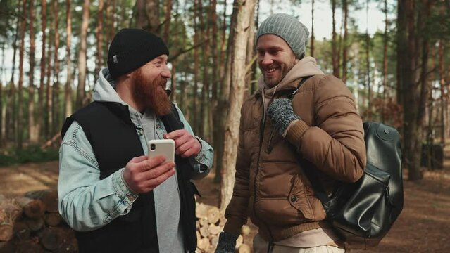 Two happy hiker friends talking and looking for the way on the map on phone in the woods with a backpack