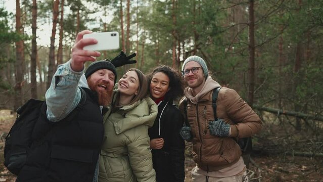 Happy multinational tourist friends taking selfies on phone in the woods
