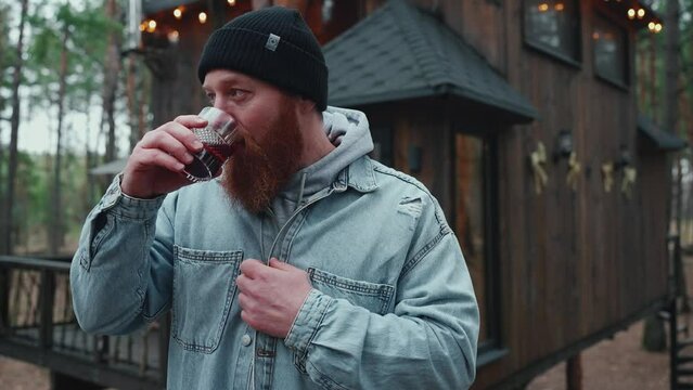 Handsome bearded redheaded tourist man drinking mulled wine in the forest