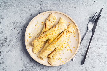 Plate of fresh crepes with orange zest on gray background