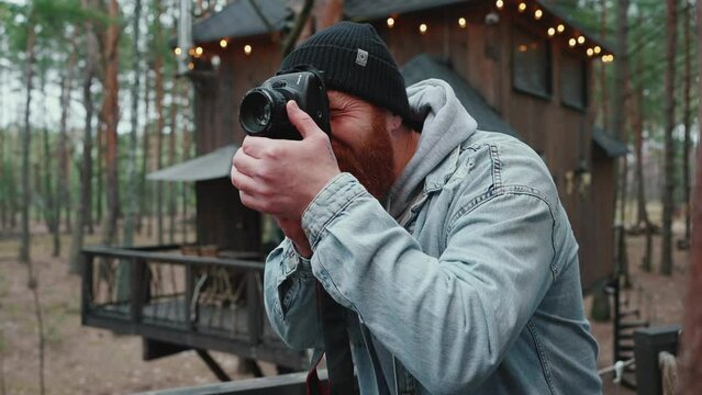 Handsome red haired man taking pictures on his camera in the forest