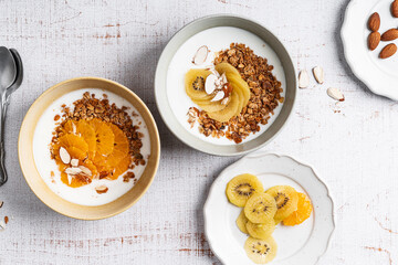 Bowls of yogurt with granola, kiwi, and orange fruits,  top view. Healthy  breakfast