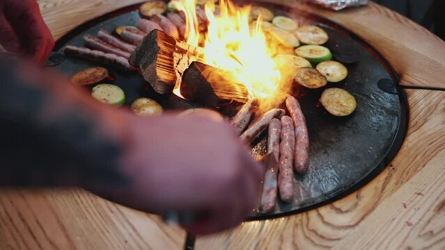 Close-up view of man frying sausages with zucchini on the fire 