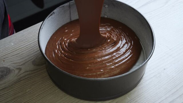Top view of liquid chocolate dough pouring into round metal mold preparing for putting cake in oven in kitchen. Confectionery, homemade food, dessert, baking, mixing ingredients, pastry, cooking.