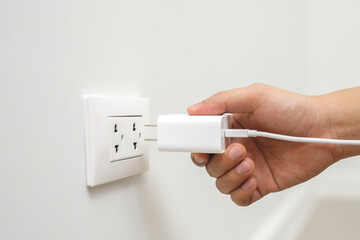 close up hand plugging adapter charge the battery with outlet socket plug and hold mobile phone on...