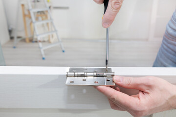 Worker installs a door hinge on a door using a screwdriver. Screw tightening. Repair in the house. Door installation. Close-up.