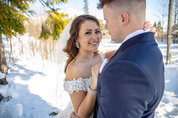 Young couple of bride and groom posing for photographer portraits in a snowy beautiful nature under high mountains High tatras on Strbske pleso with a huge hotel in behind Patria. White dress and blue