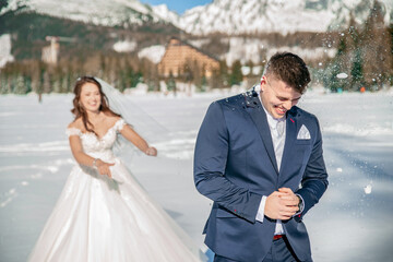 Young couple bride and groom playing in the winter nautre under snowy mountains on a frozen lake. playing snowball fight. throwing snow balls on each other. having a great time. laughing