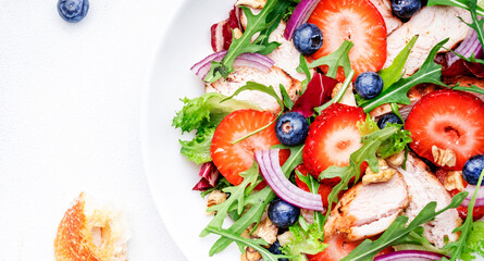 Strawberry, grilled chicken fillet and herbs healthy salad with arugula, blueberries and walnuts, white kitchen table, place for text. Fresh useful dish for healthy eating