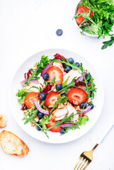 Strawberry, grilled chicken fillet and herbs healthy salad with arugula, blueberries and walnuts, white kitchen table, place for text. Fresh useful dish for healthy eating
