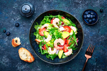 Strawberry, shrimp and herbs healthy salad with arugula, avocado and onion, blue kitchen table. Fresh useful dish for healthy eating