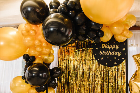 Arch decorated with black, brown, golden balloons and stars. Photo-wall decoration space, place with gold background. Trendy autumn decor. Celebration concept. Birthday party. Happy birthday text.
