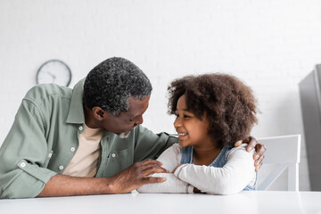 Obraz premium happy african american grandfather hugging curly granddaughter in kitchen.