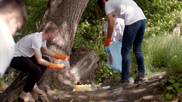 Multiracial group of young volunteers in gloves picking up garbage manually in the forest. Young men taking care of the environment, working together and helping each other