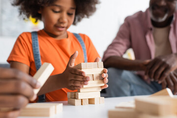 Obraz na płótnie Canvas Blurred african american kid playing wood blocks game near parents at home.