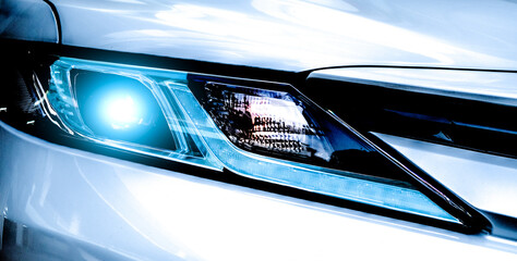 Closeup headlamp light of a white luxury car. Automotive industry concept. Electric car or hybrid vehicle concept. Automobile leasing and insurance concept. Auto leasing business. Electric vehicle.
