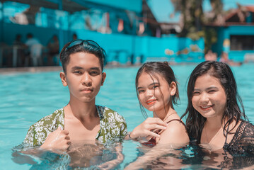 A young man with two women taking a dip at a swimming pool during the summer break.