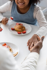 Obraz na płótnie Canvas cropped view of happy african american girl holding hands with father during breakfast.
