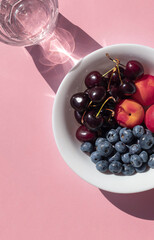 Organic ripe berries and fruits in the white bowl on the pink table. Close up