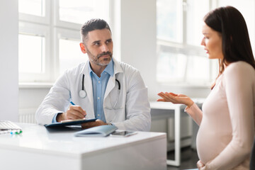 Obraz premium Gynecology consultation. Pregnant woman visiting her doctor, gynecologist listening to patient and writing in clipboard