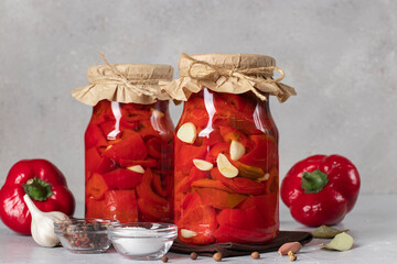 Pickled sweet peppers with garlic in two glass jar on gray background