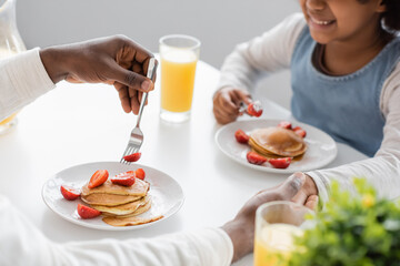 cropped view of cheerful african american girl holding hands with father during breakfast.