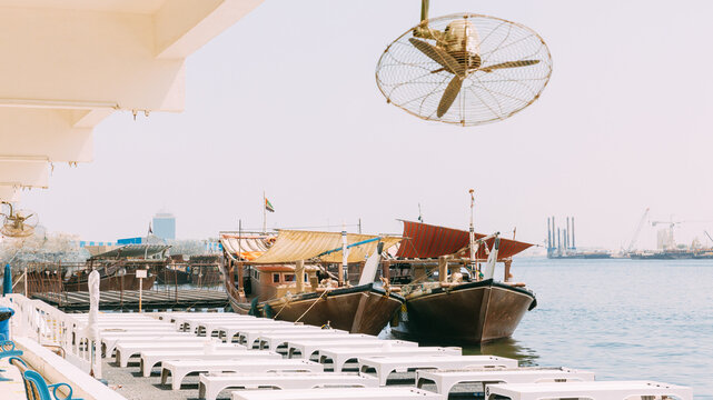 Many Dhow, sailboat, sailing vessel boat is moored to the city pier, jetty in sunny summer day. Urban city background. Port in Dubai, United Arab Emirates, UAE.