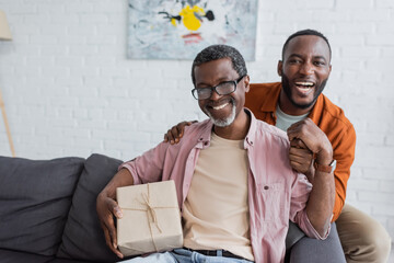 Cheerful african american middle aged man holding gift near son during father day celebration at...