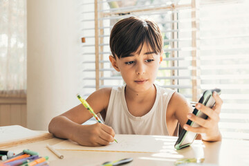 Child drawing in a bright home copying an image from a cell phone. Concept of creativity, technology and learning.