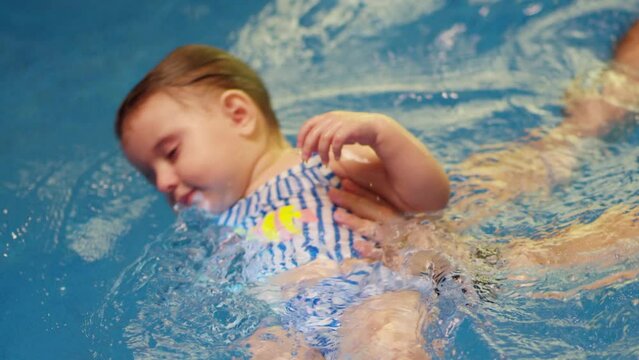 Father holding little baby and helping to swim in swimming pool with clean blue water. Professional water therapy for kids . Swimming training from an early age . Parent having fun . Happy lifestyle