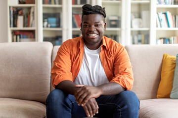 Happy young black man sitting on couch at home