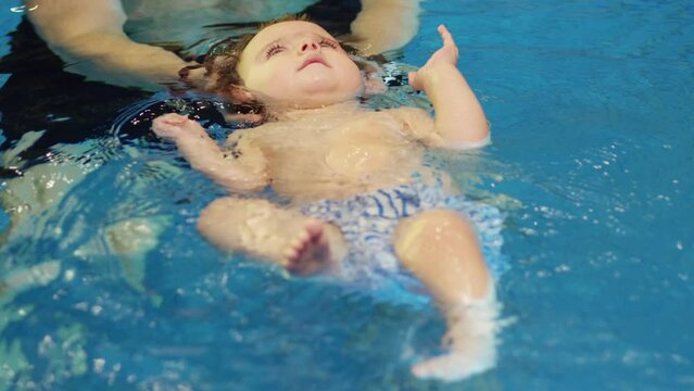 Father holding little baby and helping to swim in swimming pool with clean blue water. Professional water therapy for kids . Swimming training from an early age . Parent having fun . Happy lifestyle