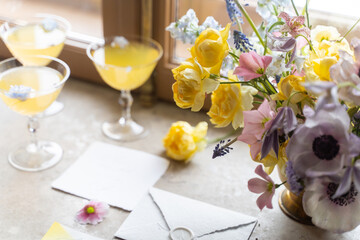 Gentle wedding floral decoration composition bouquets of flowers over white invitation and glasses with cocktails . Top view. Selective soft focus. Copy space, negative space for design advertisement