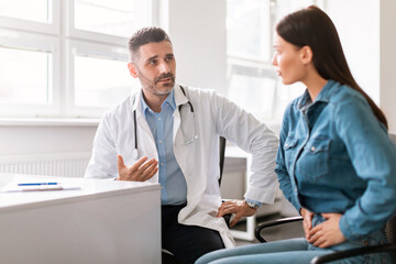 Male medical specialist consulting female patient, complaining at abdominal pain, clinic interior