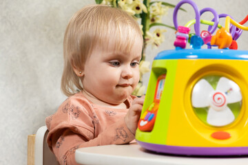 A one-and-a-half-year-old girl plays with a musical glowing toy, presses buttons. Children's development, toys for babies