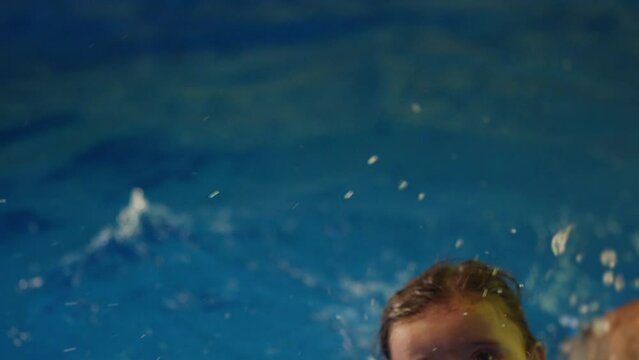 Father holding little baby and helping to swim in swimming pool with clean blue water. Professional water therapy for kids . Swimming training from an early age . Parent having fun . Happy lifestyle