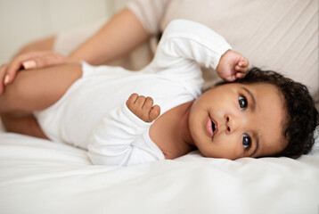 Fototapeta na wymiar Sweet cute little african american baby lies on soft bed with mom, rest and relax, enjoy free time at home, close up