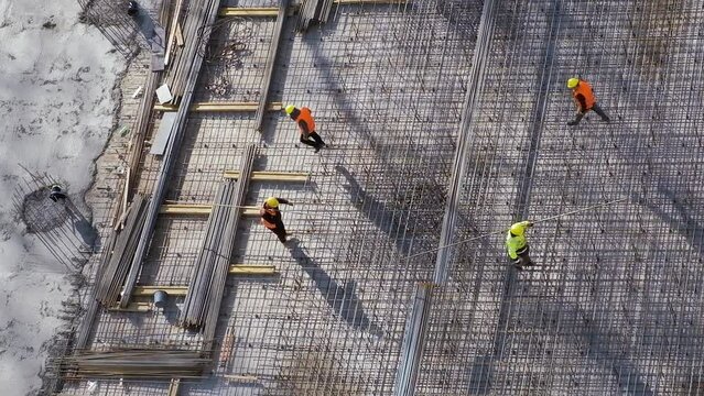 Workers carrying metal bars stepping on reinforcement rebars above slab floor