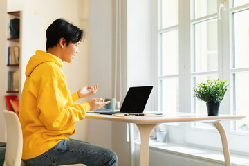 Cheerful Asian Teen Guy Video Calling Via Laptop At Home - obrazy, fototapety, plakaty