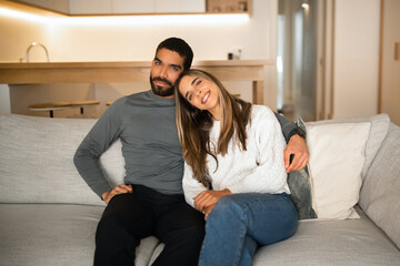 Obraz premium Happy international millennial couple hugging, sit on sofa, enjoy free time together, watch tv in minimalist living room