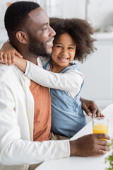 curly african american girl smiling while hugging happy father at home.