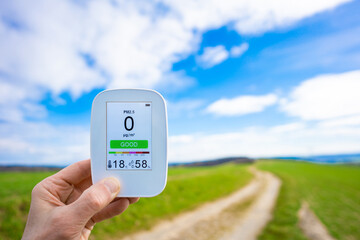  hand holding an air quality detector against the backdrop of a beautiful summer landscape. The...