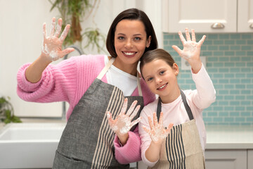 Happy european millennial female and little girl in aprons cook cookies, show hands with flour,...