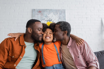 African american father and grandfather kissing cheerful child in living room.