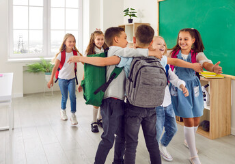 Group of little school friends hug each other tightly as they arrive at school before classes. Joyful and funny boys and girls with backpacks on their shoulders meet at school. Back to school cocept.